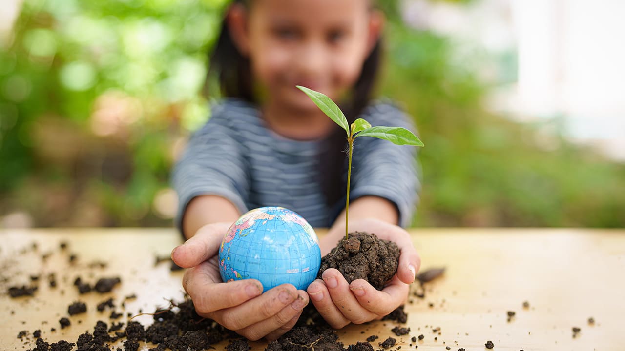 Nachhaltigkeit - Mädchen hält Weltkugel und Pflanze in den Händen
